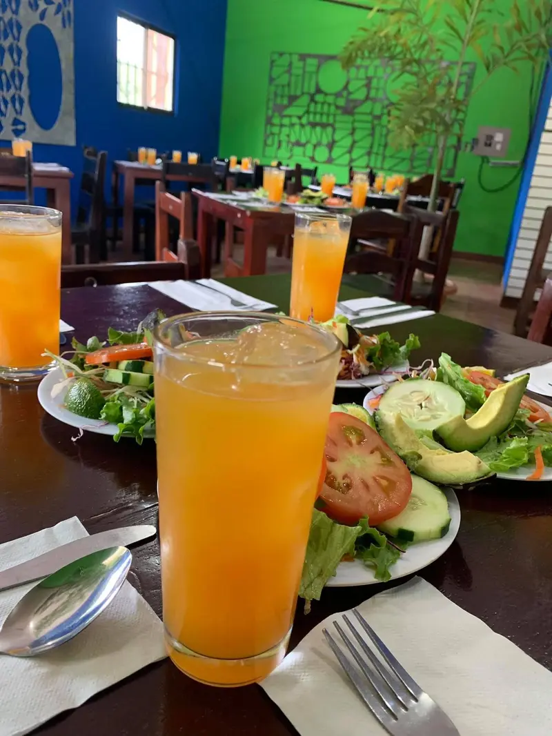 Vaso de fresco de naranja junto a platos de ensalada con aguacate, tomate y pepino en una mesa del salón
