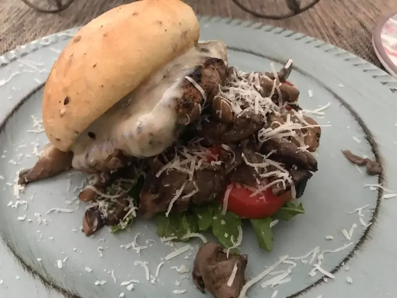 Pan casero con carne, queso derretido, hongos salteados y parmesano sobre rúcula y tomate
