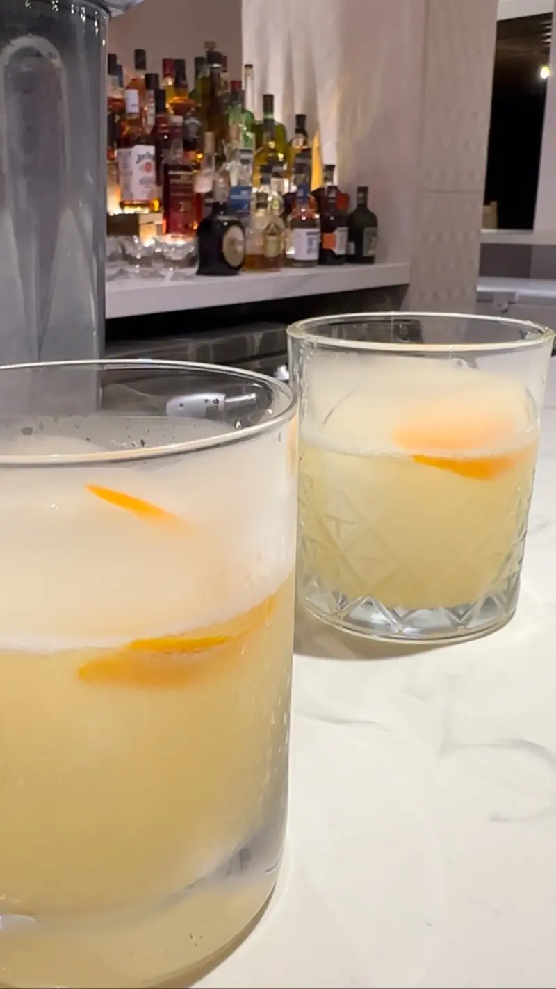 Dos cócteles cítricos con hielo frente a la barra y la estantería de licores