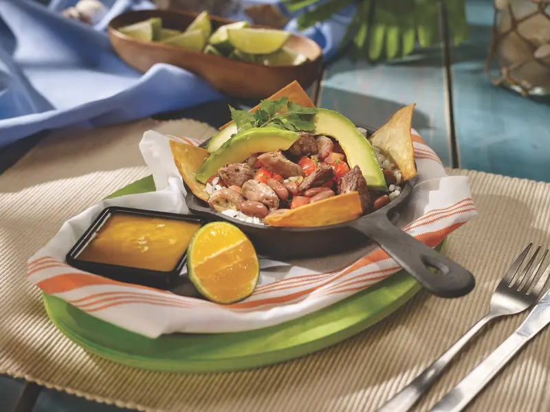 Cazuela de hierro con carne, frijoles y aguacate, con una salsa y medio limón al lado