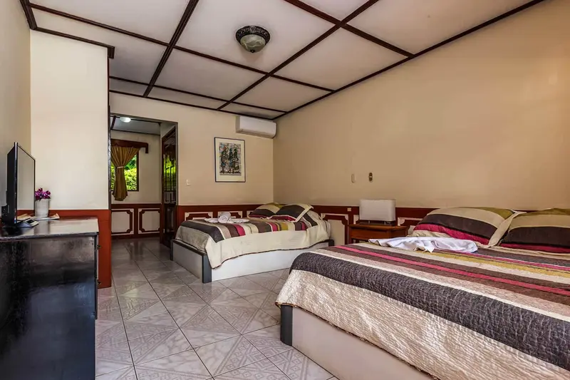 Habitación con dos camas, televisor, aire acondicionado y techo de madera con vigas