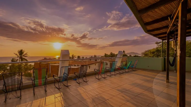 Terraza de la azotea con deck de madera y hamacas al atardecer, con el pueblo y el mar al fondo