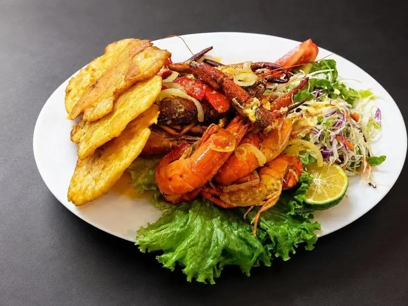 Plato con langostinos a la plancha, patacones, repollo y limón sobre un plato blanco