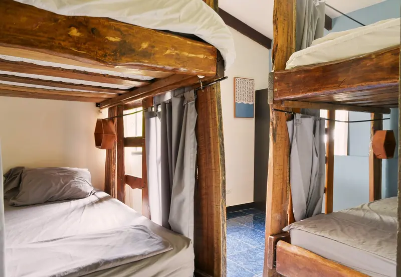 Dormitorio compartido con literas de madera rústicas y cortinas, luz natural y piso azul