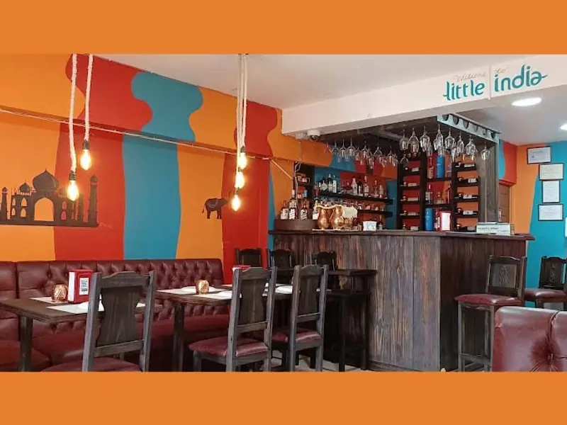 Interior del restaurante con barra de madera, paredes naranjas y azules y banquetas de cuero