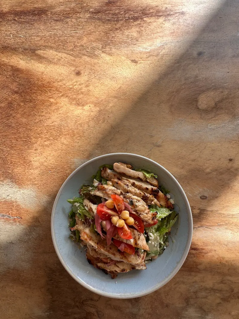 Bowl con ensalada de pollo a la parrilla, garbanzos y tomate sobre una mesa de madera