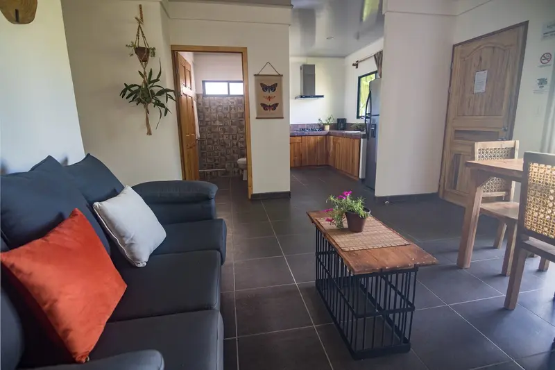 Sala con sofá gris, mesa de centro y comedor, con cocina al fondo