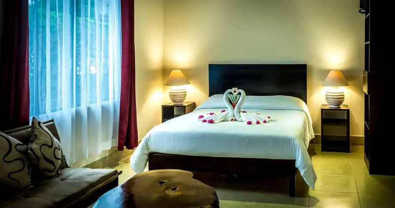 Habitación con cama matrimonial, toallas en forma de cisnes y ventanal con cortinas turquesa