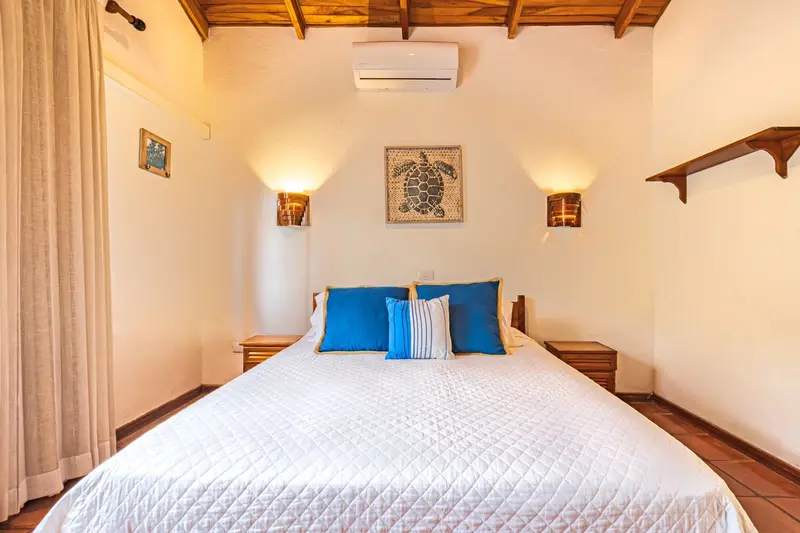 Cama king con almohadas azules, mesitas de noche de madera y lámparas