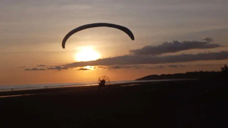 Paramotor volando sobre la playa al atardecer, con el parapente y el sol al fondo