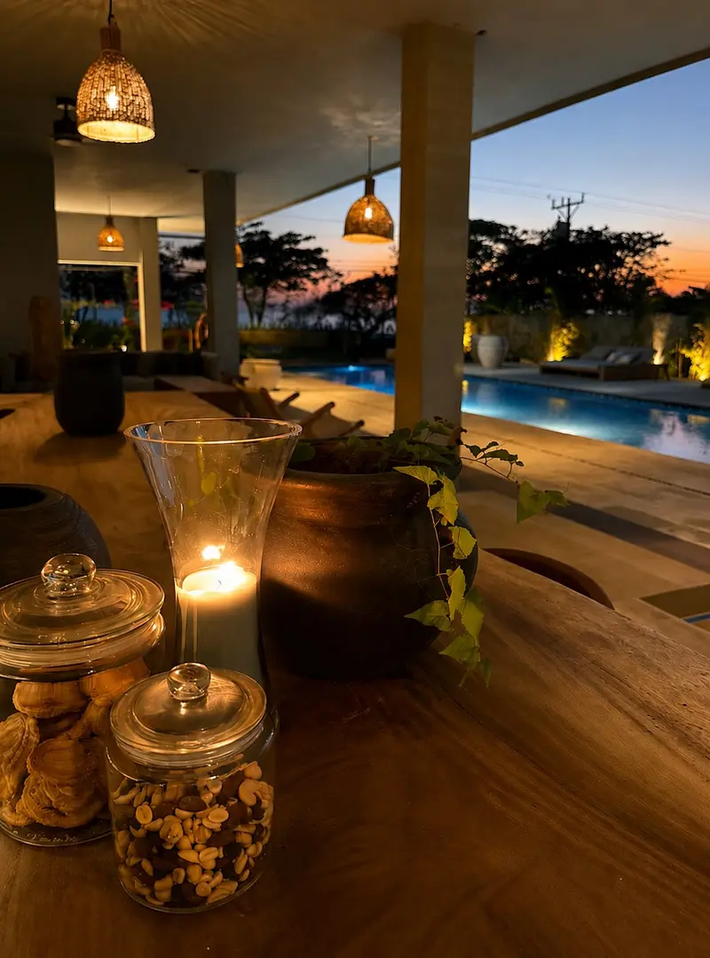 Vela y frascos sobre una mesa de madera con la piscina y el atardecer al fondo
