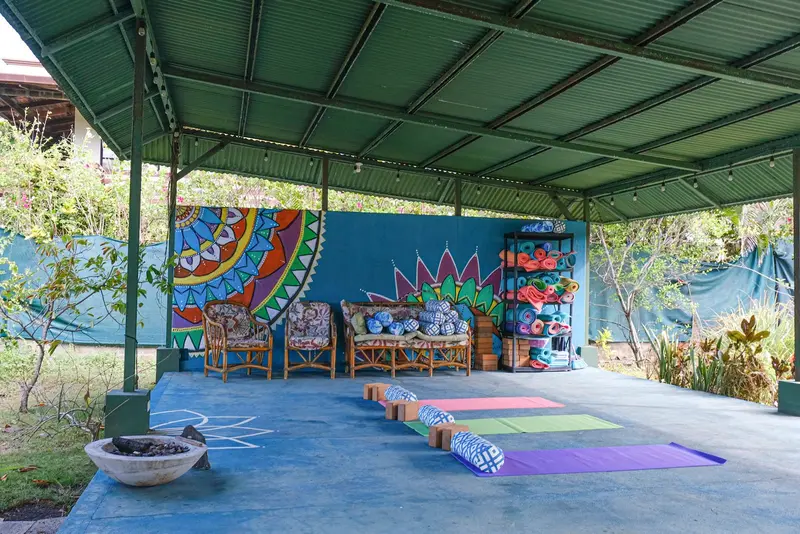 Pabellón techado con esterillas de yoga frente a un mural de colores
