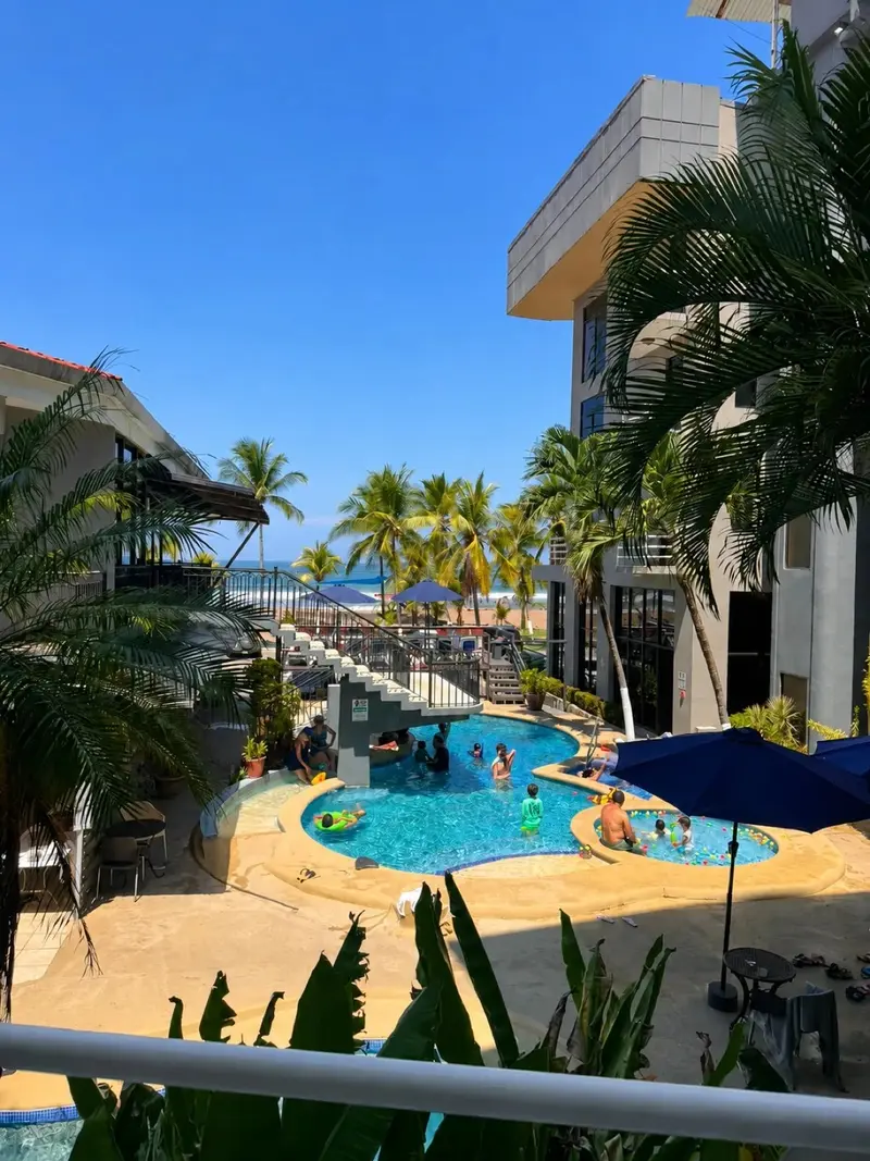 Vista desde el balcón hacia la piscina, las palmeras y la playa