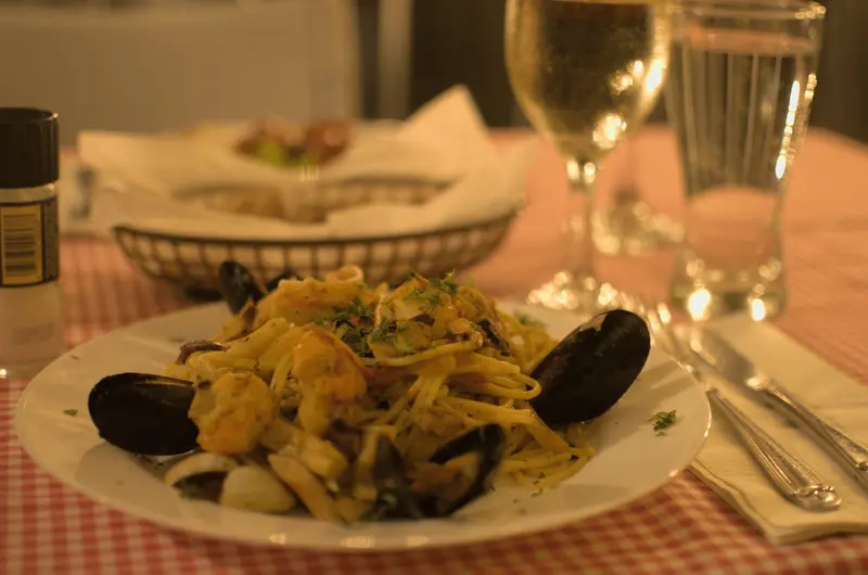 Pasta con mejillones en un plato blanco sobre mantel de cuadros, con copas al fondo