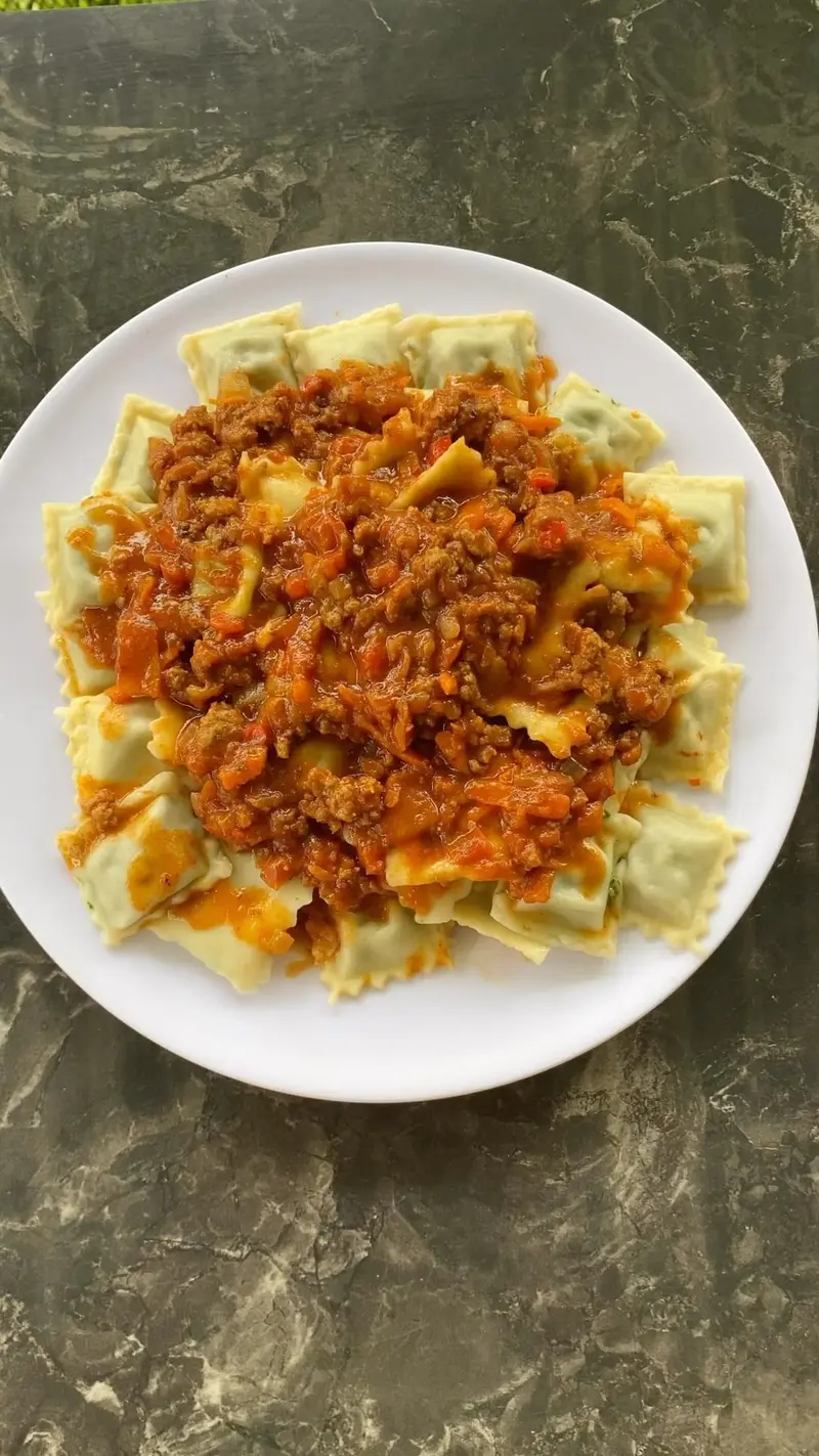 Ravioles con salsa roja de carne sobre un plato blanco