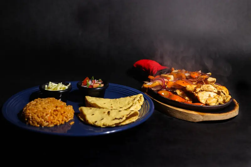 Plato de carne con pimientos, tortillas, arroz y salsas sobre una mesa oscura