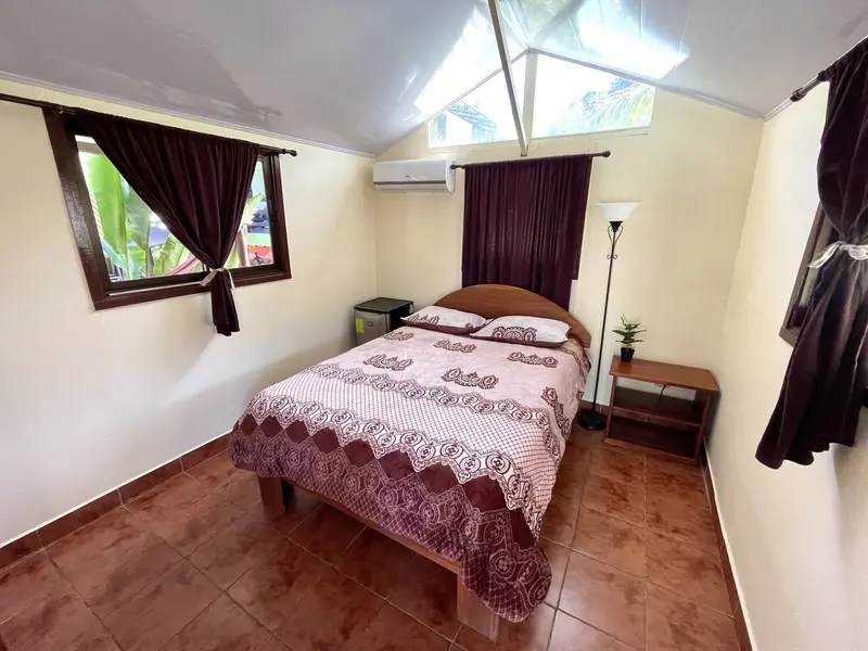 Habitación con cama matrimonial de colcha estampada, cortinas oscuras y aire acondicionado en la pared
