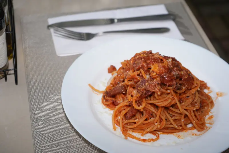 Plato de espagueti con salsa de tomate sobre una mesa con cubiertos y servilleta