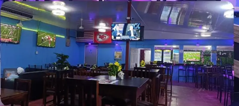 Salón con mesas de madera, banderas y televisores en la pared azul