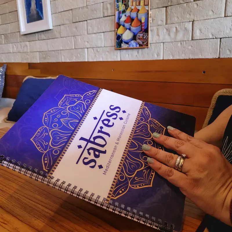 Menú de Sabress con tapa azul y mandala dorada sobre una mesa de madera