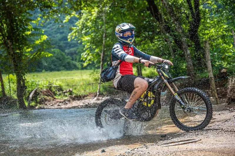 Piloto salpicando agua al cruzar un río con su moto eléctrica