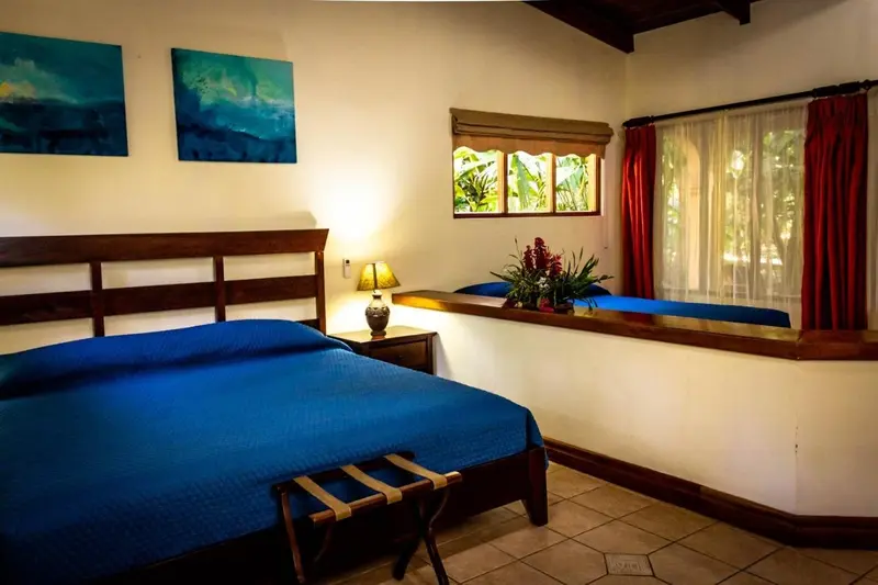 Habitación con cama azul, cabecera de madera y ventanas al jardín