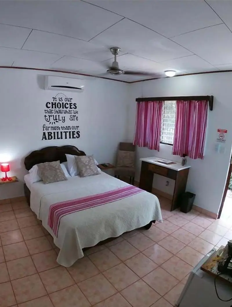 Habitación con cama de colcha rosada, ventilador de techo, cortinas rosadas y piso de baldosa