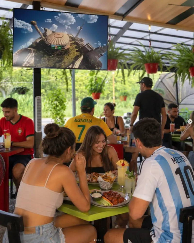 Comensales con camisetas de fútbol viendo la pantalla en el patio techado de D'Corner