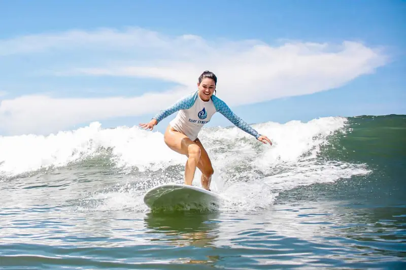 Mujer con camiseta de licra surfeando una ola pequeña