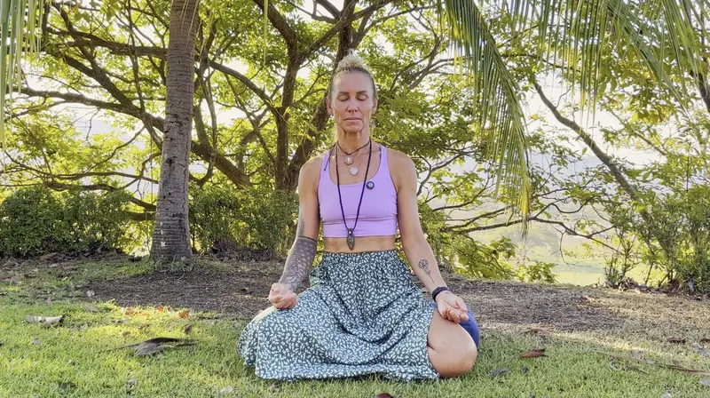 Victoria meditando sentada sobre el césped bajo árboles con vista al valle