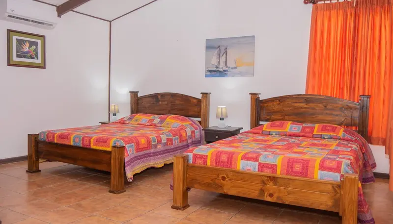 Habitación con dos camas con cobijas de colores y cortinas naranjas