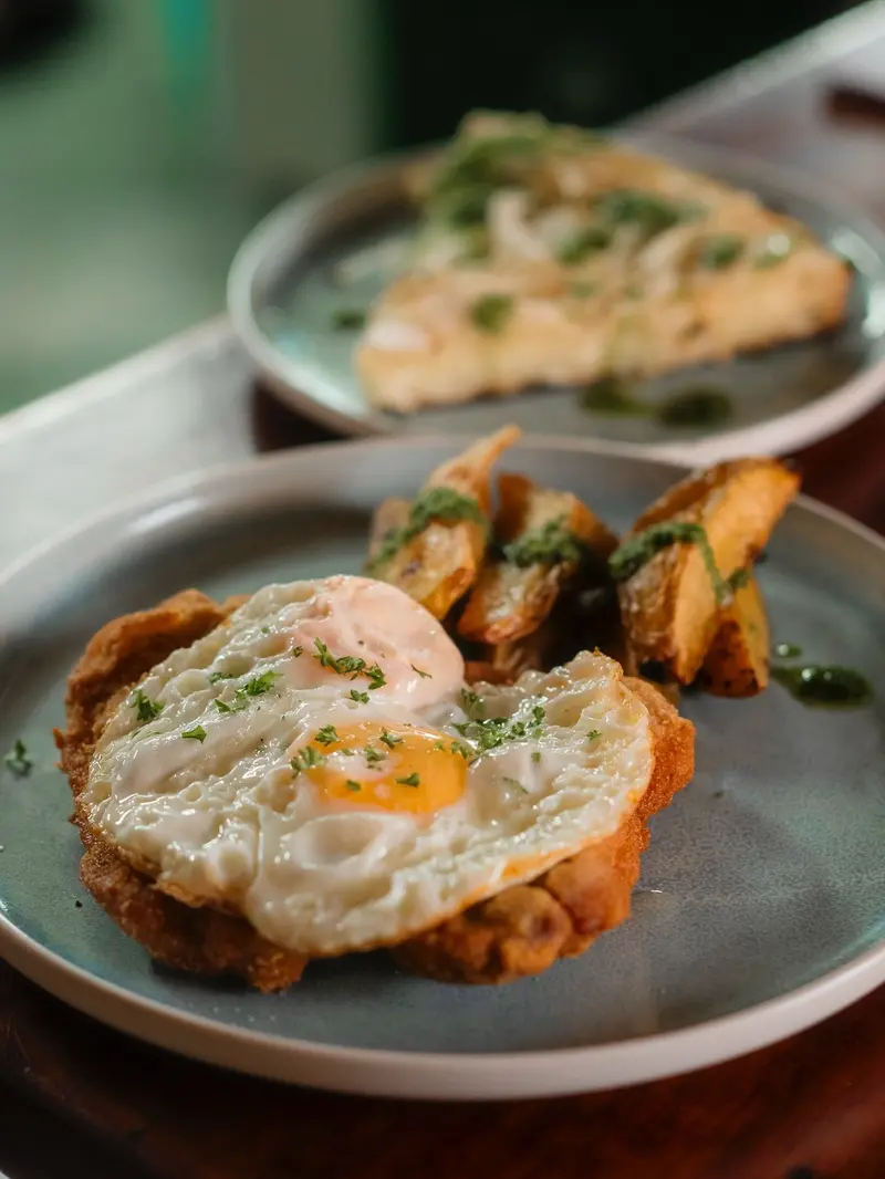 Huevo frito sobre una base crocante y otro plato con tortilla, en platos de cerámica