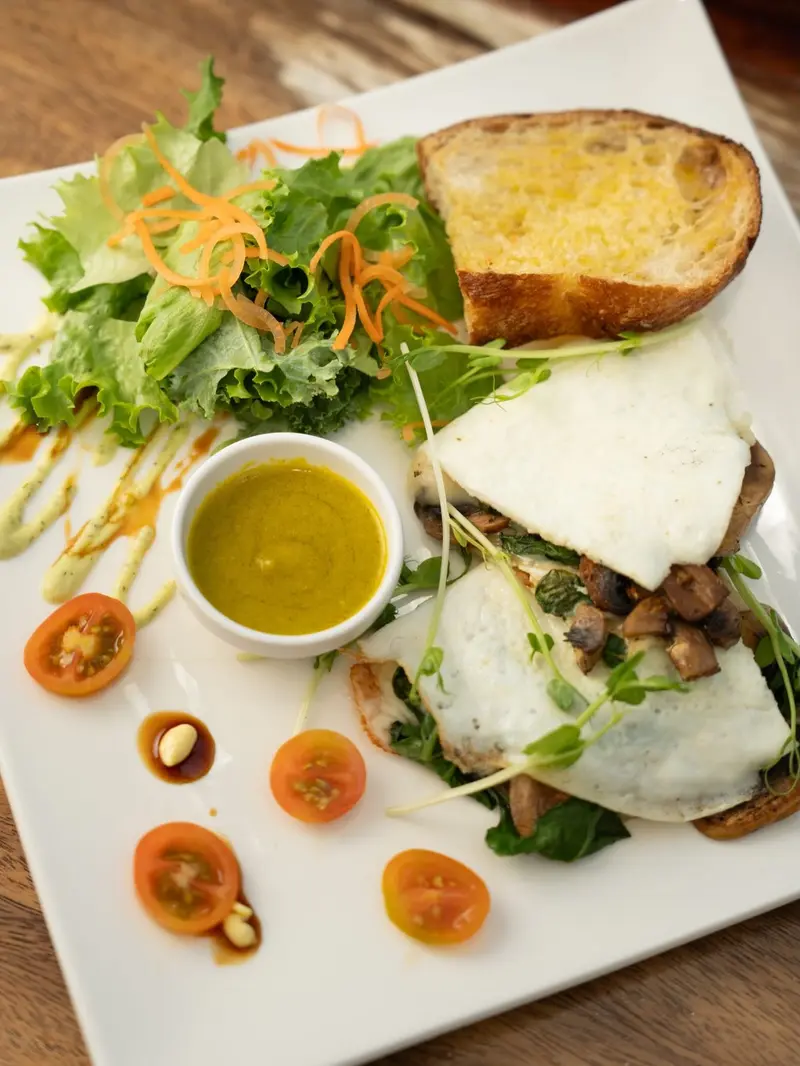 Plato cuadrado con ensalada, pan tostado y sándwich abierto con huevo, hongos y salsa