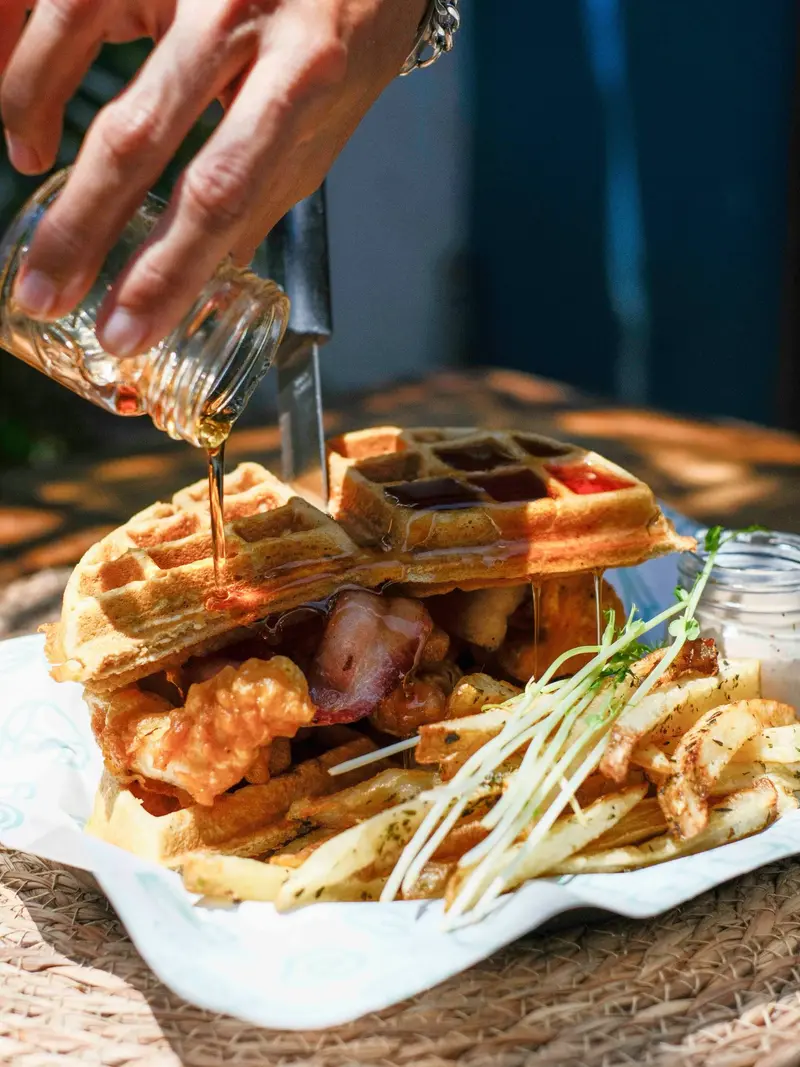 Waffle con pollo crujiente y papas fritas mientras se vierte jarabe