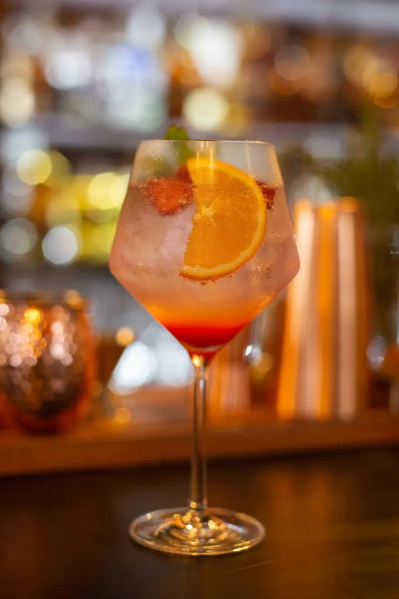 Cóctel rosado con una rodaja de naranja en copa de vino sobre la barra