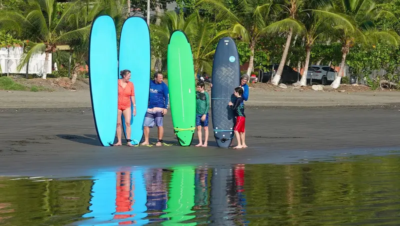 Grupo en una playa de arena oscura con cinco tablas de colores paradas en fila