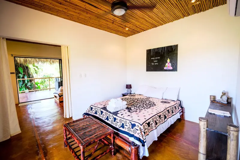 Habitación con cama de madera, piso de madera y ventana con vista a la vegetación