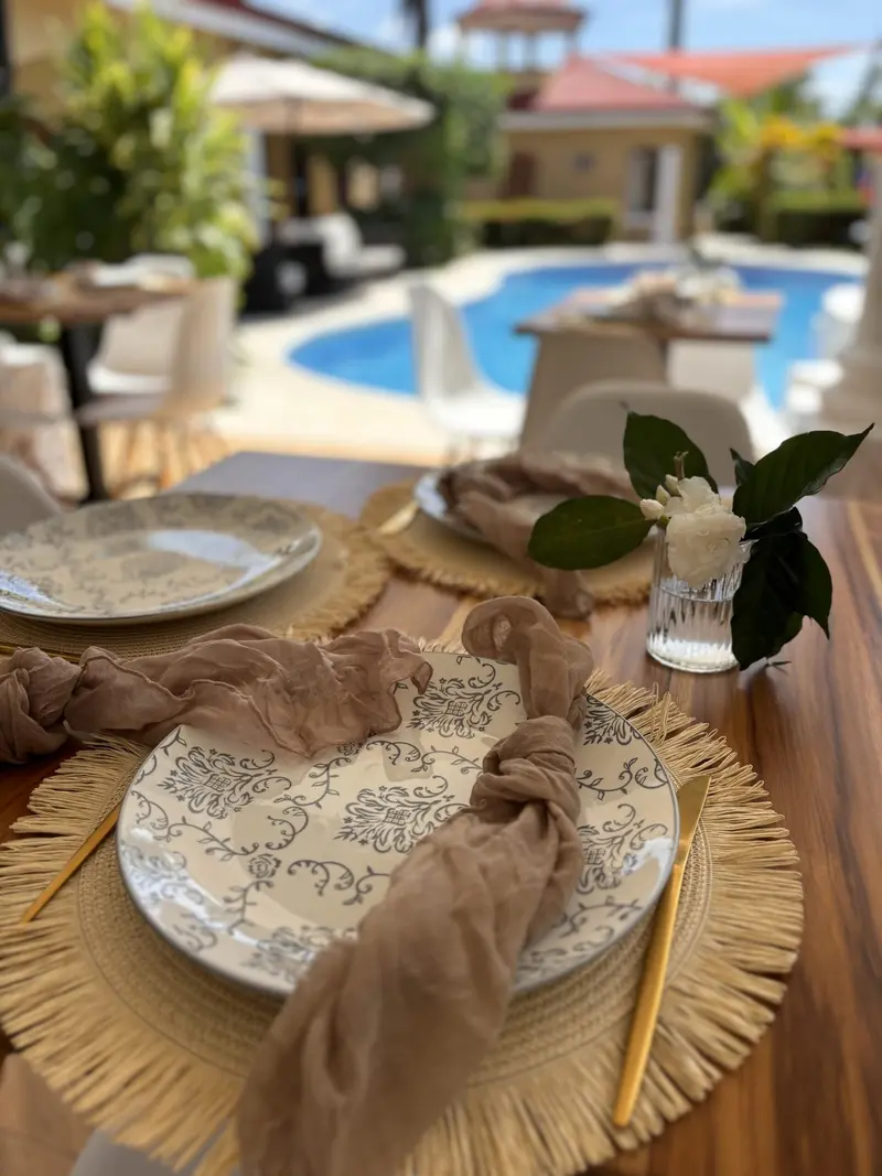 Mesa del restaurante SWAY con platos decorados y servilleta, y la piscina del resort al fondo