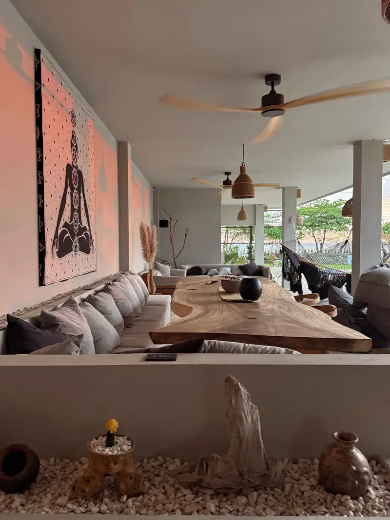 Terraza techada con una larga mesa de madera, sofás con almohadones y una hamaca frente al mar