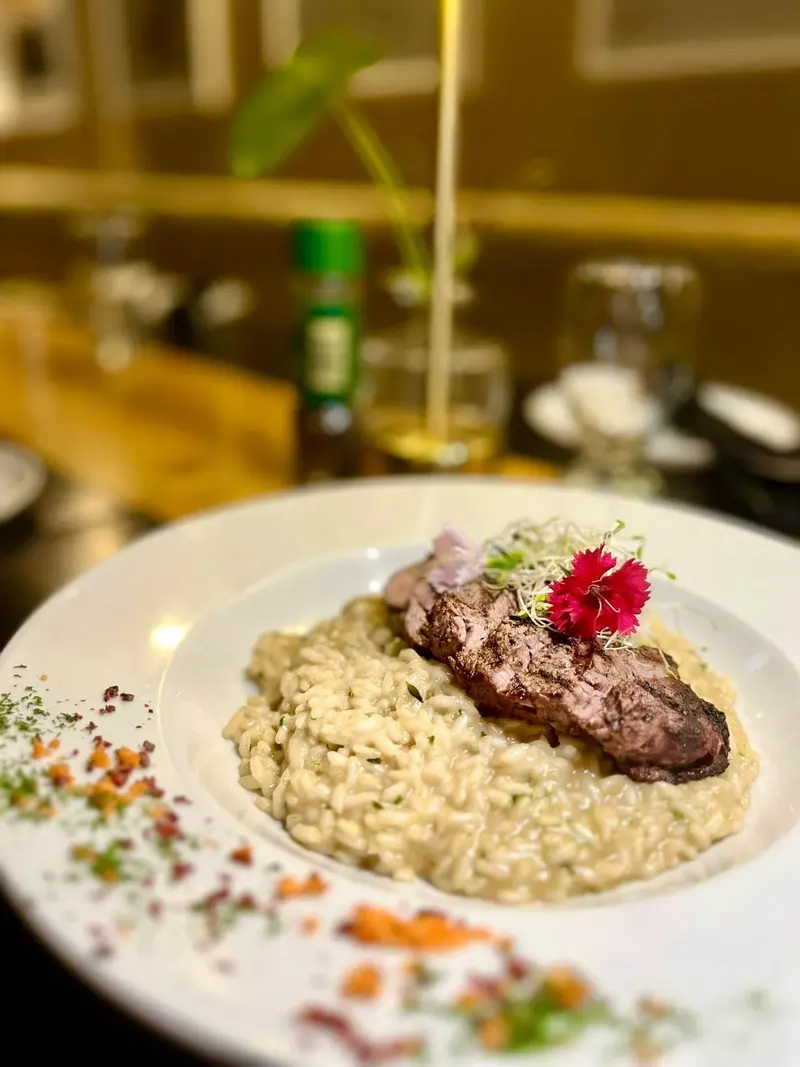 Risotto cremoso con un medallón de carne y una flor roja sobre un plato blanco