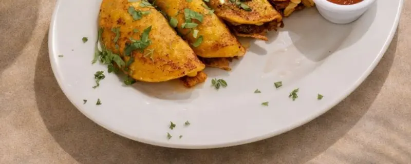 Plato de tacos dorados con salsa roja en un tazón pequeño