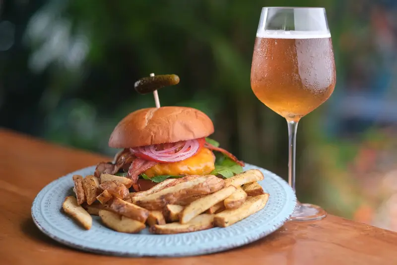 Hamburguesa con papas fritas caseras y un vaso de cerveza sobre una mesa de madera