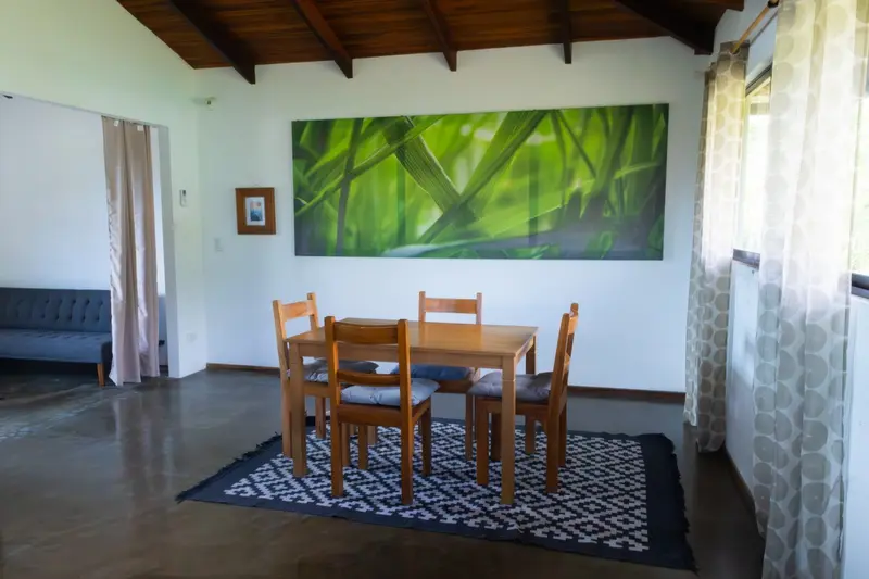 Sala-comedor de un apartamento con mesa de madera, cuatro sillas y un cuadro verde en la pared