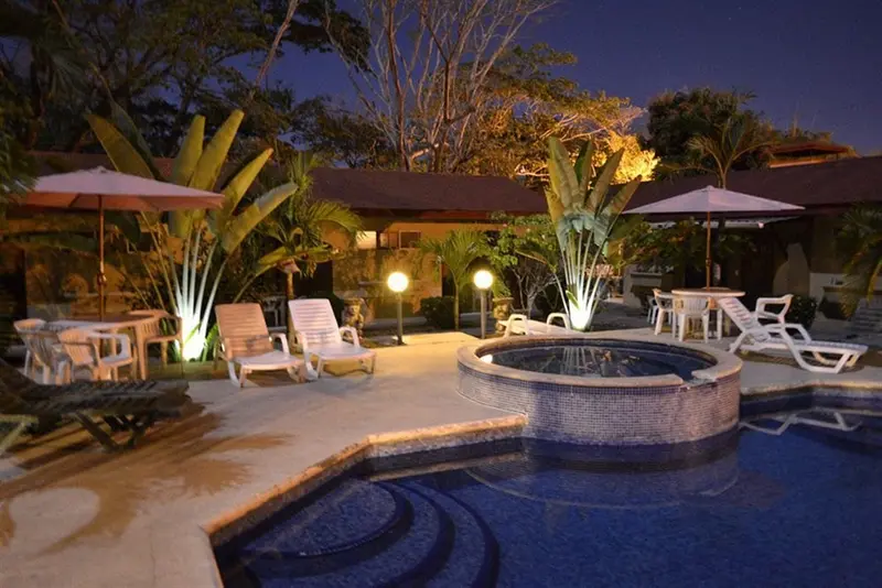Piscina y jacuzzi iluminados de noche con sombrillas y reposeras