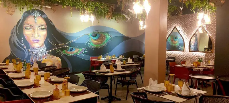 Salón con mesas puestas y un mural de una mujer con plumas de pavo real en la pared del fondo