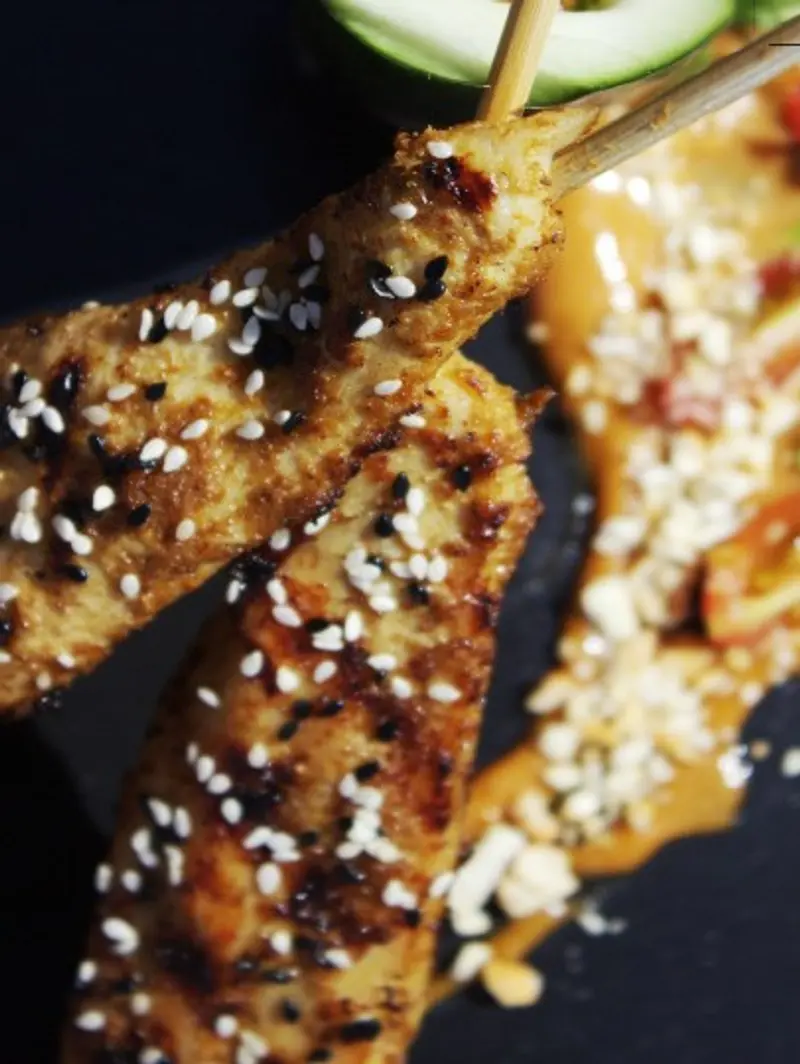 Brochetas de pollo con semillas de sésamo y salsa de maní sobre un plato oscuro