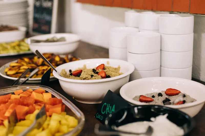 Buffet de desayuno con fruta fresca, bowls de avena y cuencos blancos apilados