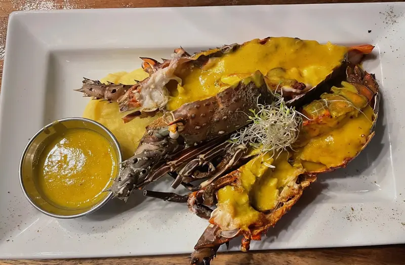 Langosta abierta con salsa amarilla sobre un plato blanco rectangular, con una salsera aparte