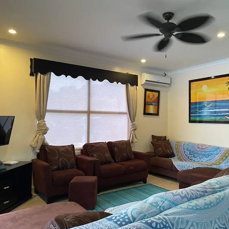 Sala de una unidad con sofás, ventilador de techo y cortinas oscuras