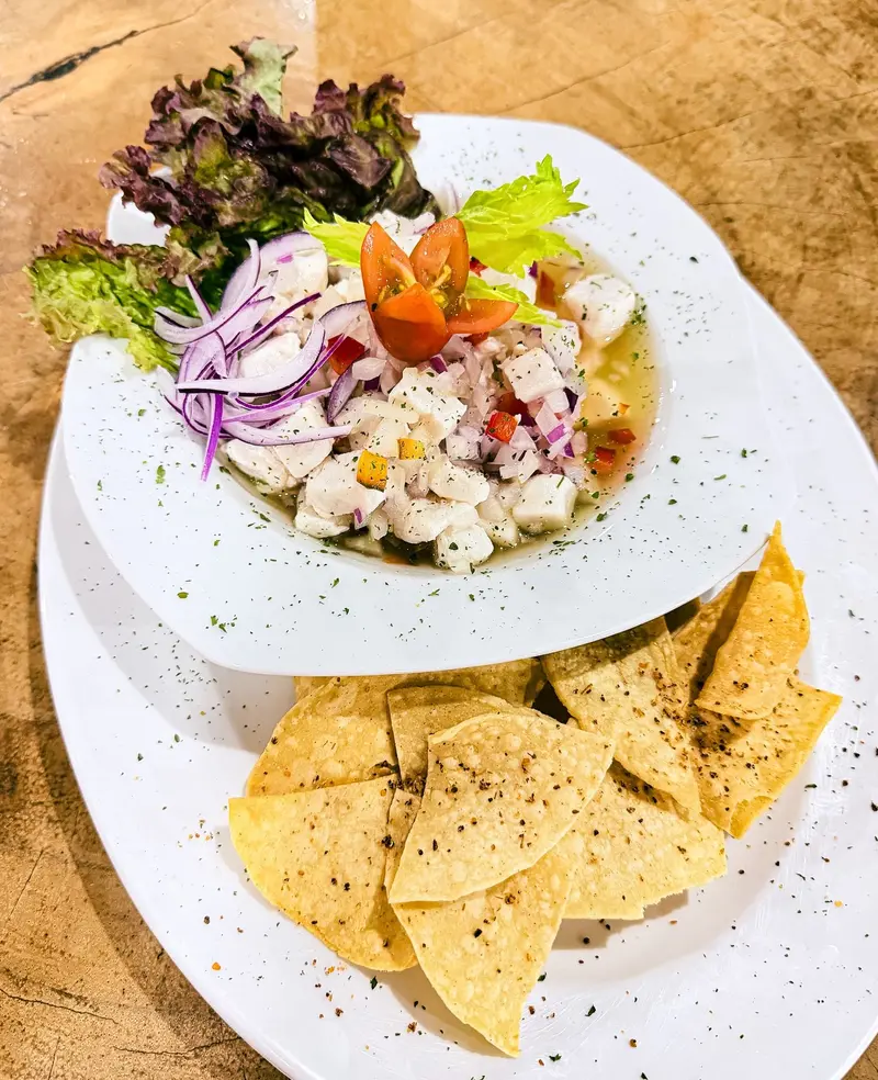 Ceviche con cebolla morada, apio y zanahoria en un plato blanco, con chips de tortilla